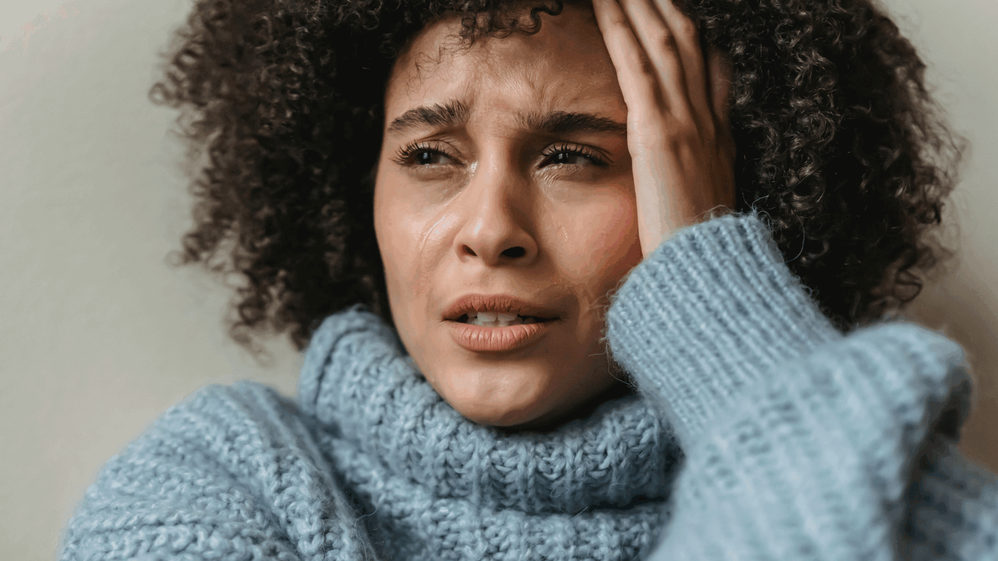 Woman of colour sat holding her head with tears streaming down her face.