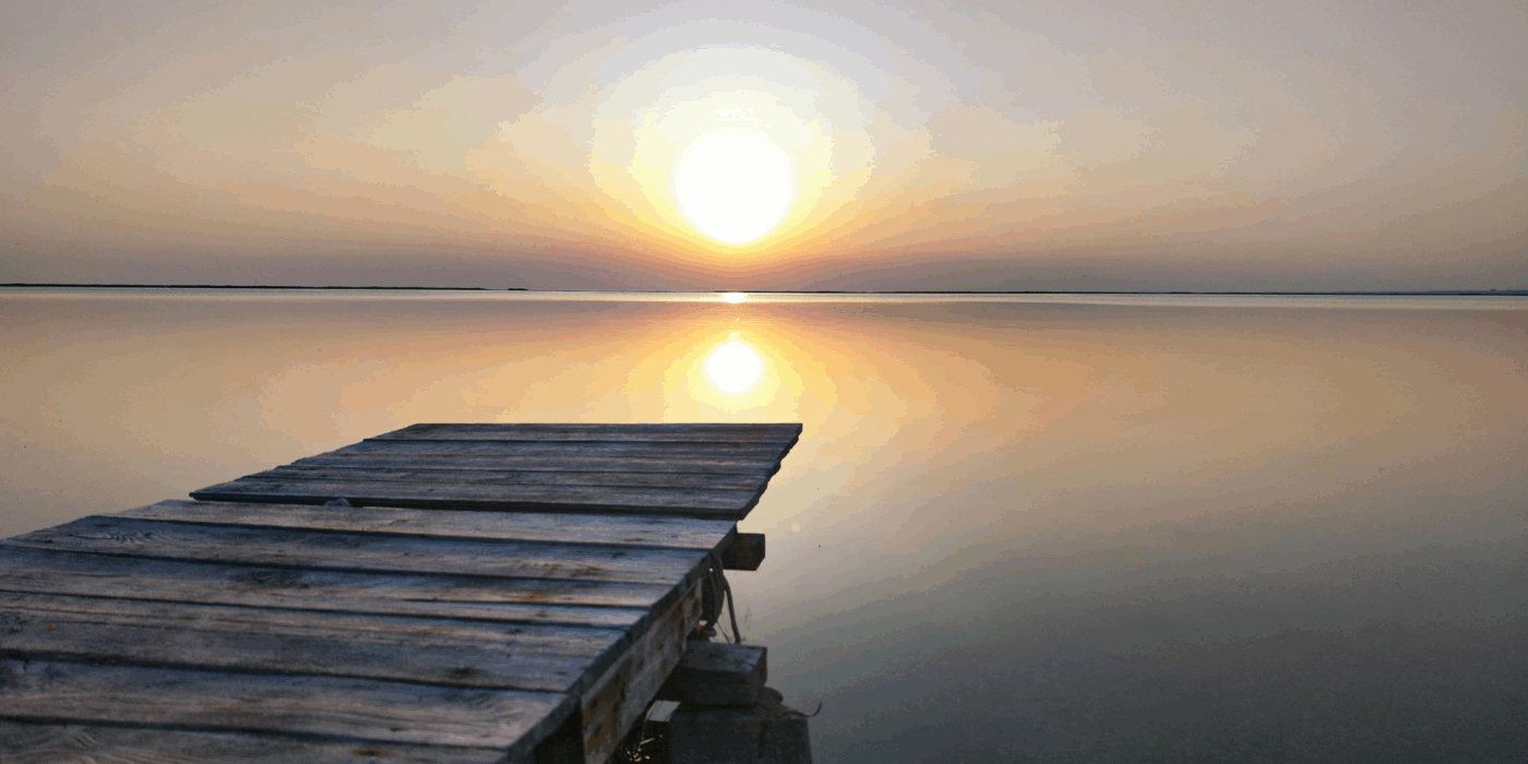 A still lake in the sunset with a wooden jetty.