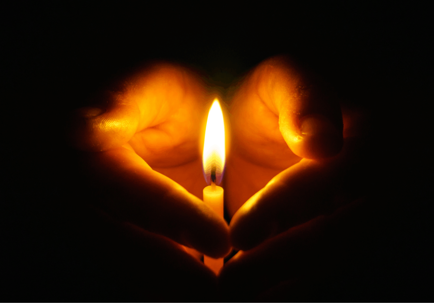 Hands in darkness holding a candle with soft light glow.