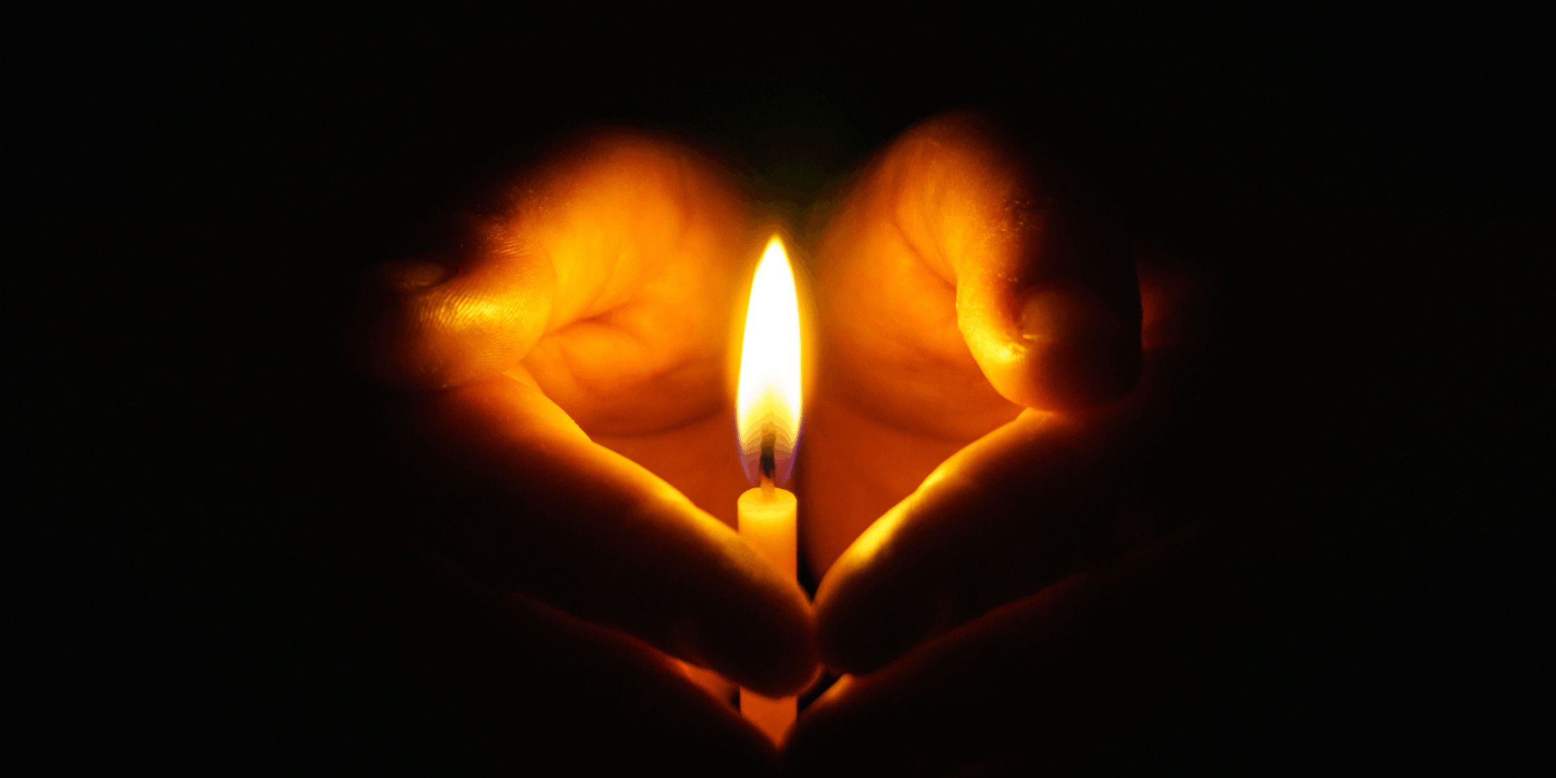 Hands in darkness holding a candle with soft light glow.