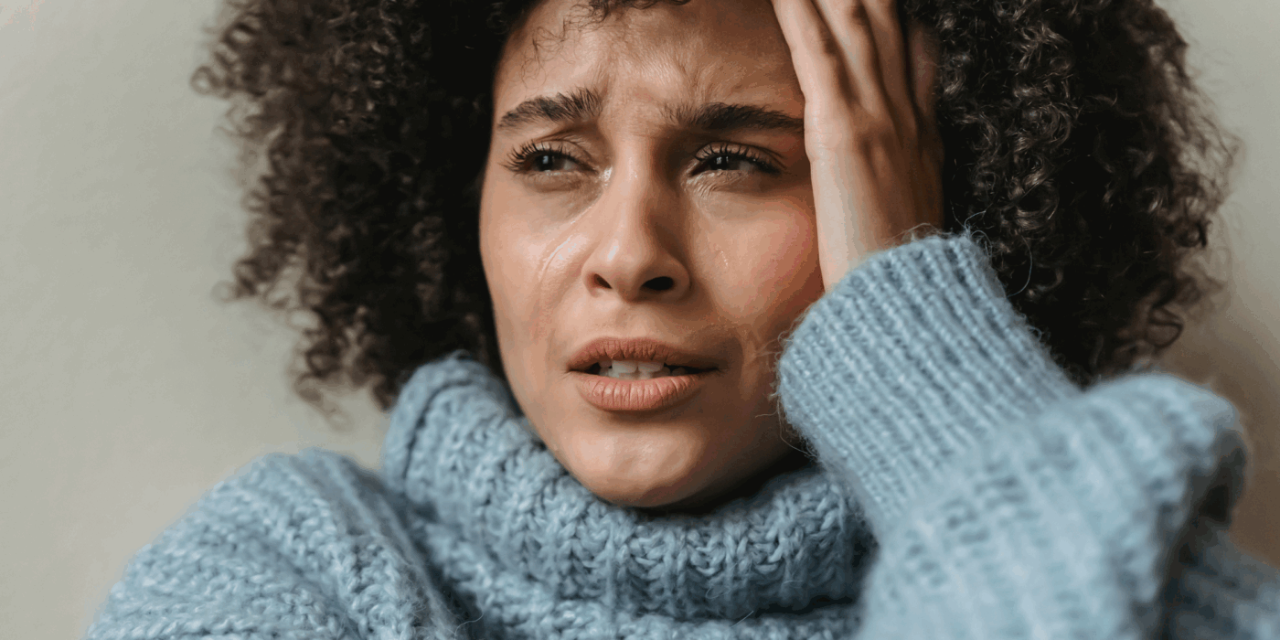 Woman of colour sat holding her head with tears streaming down her face.