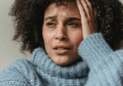 Woman of colour sat holding her head with tears streaming down her face.