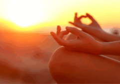 Feminine hands in a meditative pose with an orange sunset in the background.