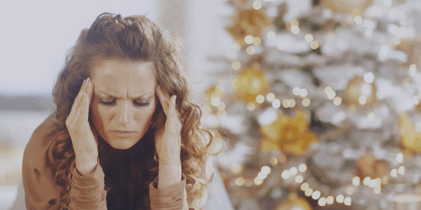 Woman looking tired and frustrated in front of a glowing christmas tree.