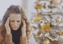 Woman looking tired and frustrated in front of a glowing christmas tree.