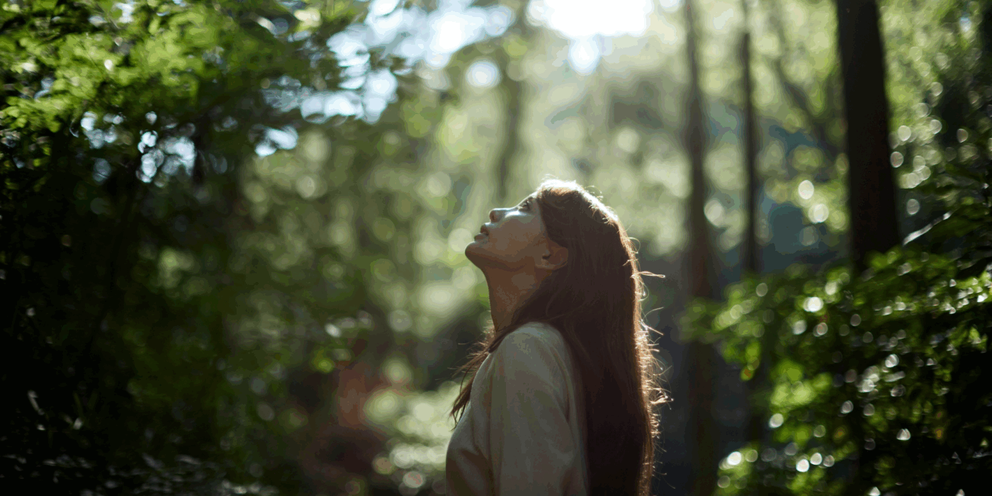 Eastern woman surrounded by trees looking up through to the sky.