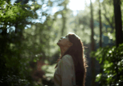 Eastern woman surrounded by trees looking up through to the sky.