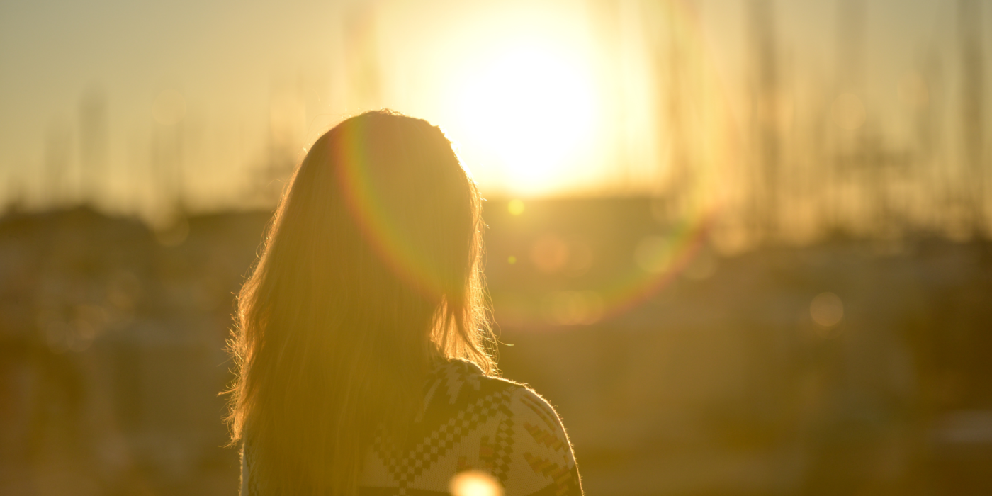 Woman standing and looking off into the distance at a sunset.