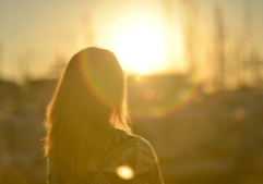 Woman standing and looking off into the distance at a sunset.