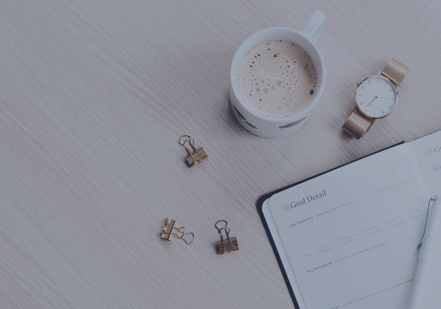 Bids eye view of a desk with a cup of coffee, watch and planner open.