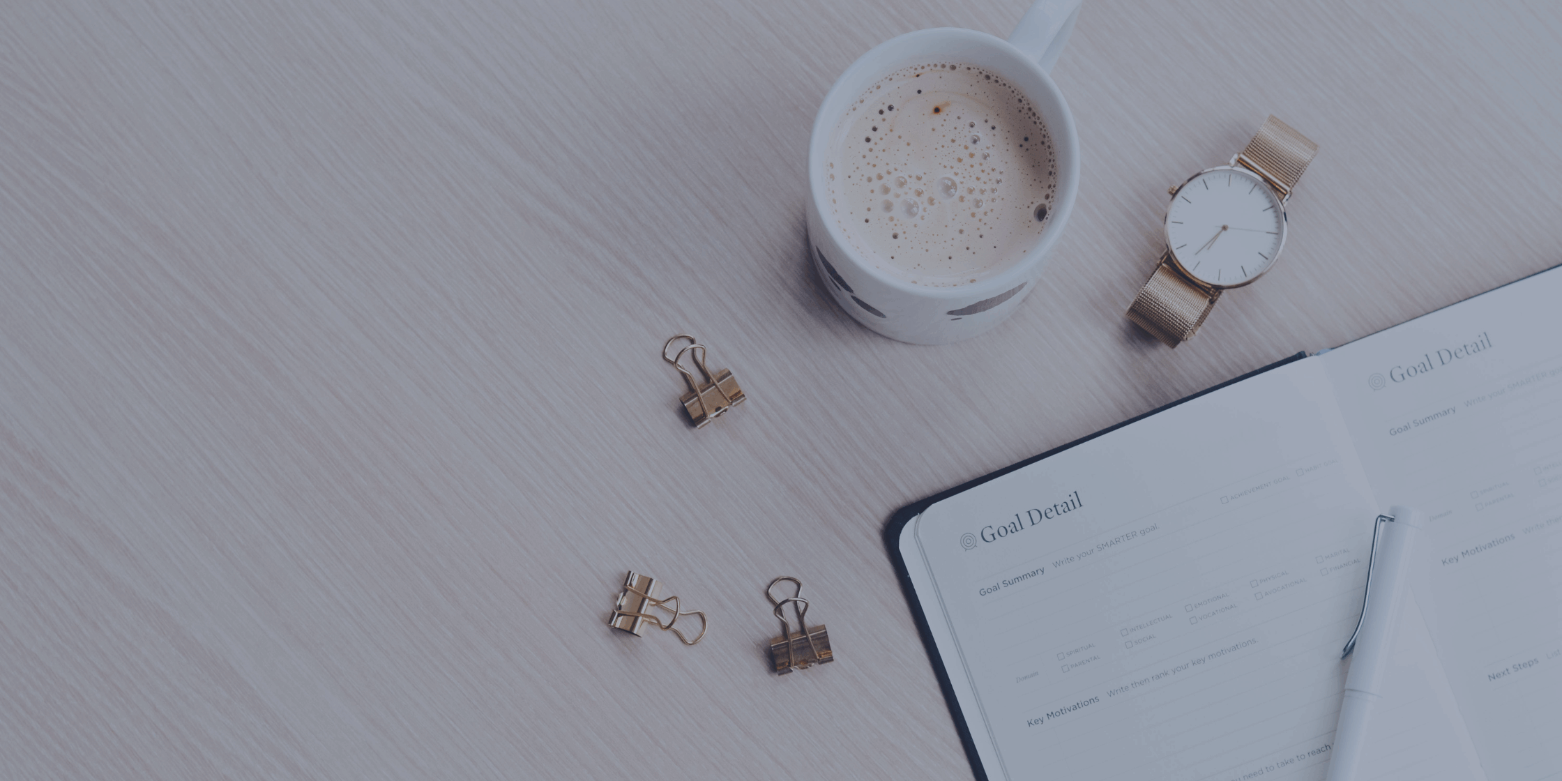 Bids eye view of a desk with a cup of coffee, watch and planner open.