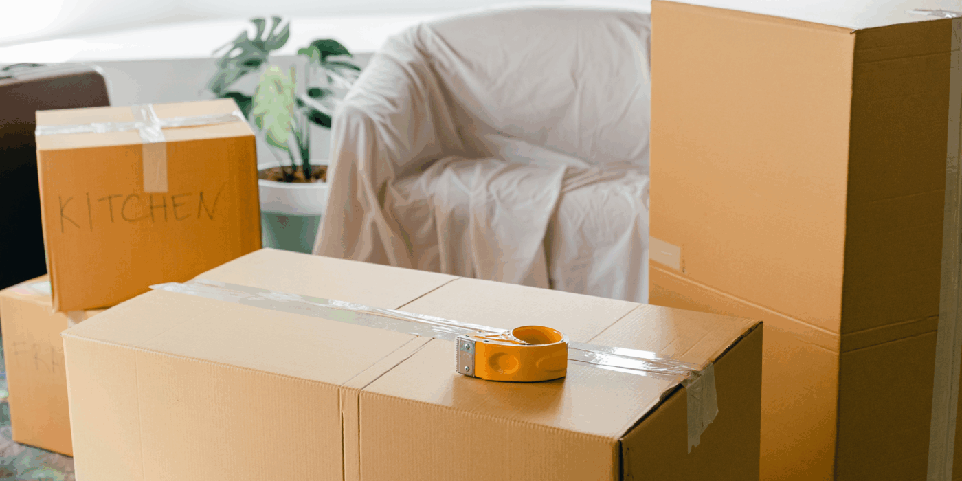 A close up shot of moving boxes with sofa and plant in background and texrt overlay 'Holding it all together, during big life shifts'.